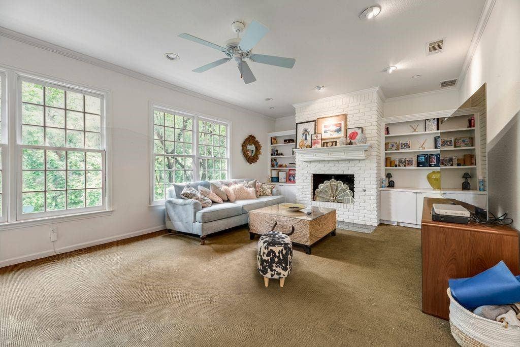 1418 Yakimo Drive, Dallas, TX 75208 Living area featuring a floor-to-ceiling painted brick fireplace, built-in shelving, crown molding, multi-pane windows, and a ceiling fan