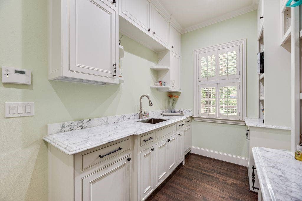 1418 Yakimo Drive, Dallas, TX 75208 White shaker-style cabinetry with matte black hardware, stone countertops with integrated backsplash, stainless steel under-mount sink, plantation shutters, and wood-finish flooring