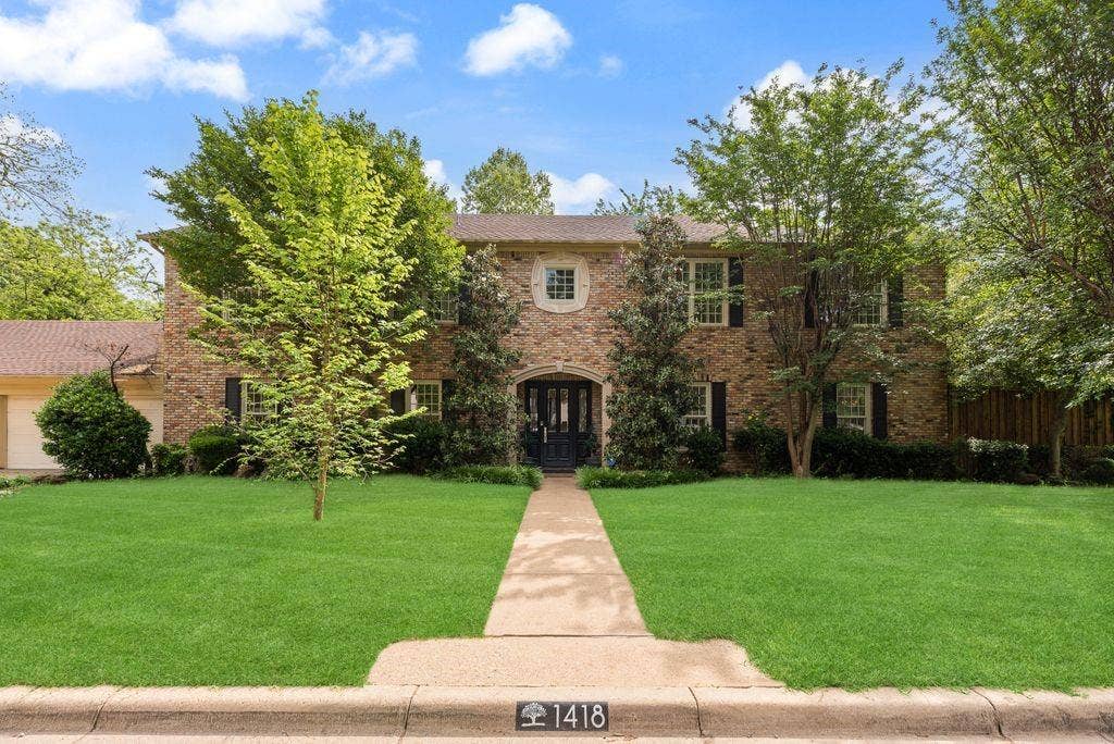 1418 Yakimo Drive, Dallas, TX 75208 Two-story brick exterior featuring a decorative stone-trimmed focal window, an arched entryway with a paneled door, and a concrete walkway