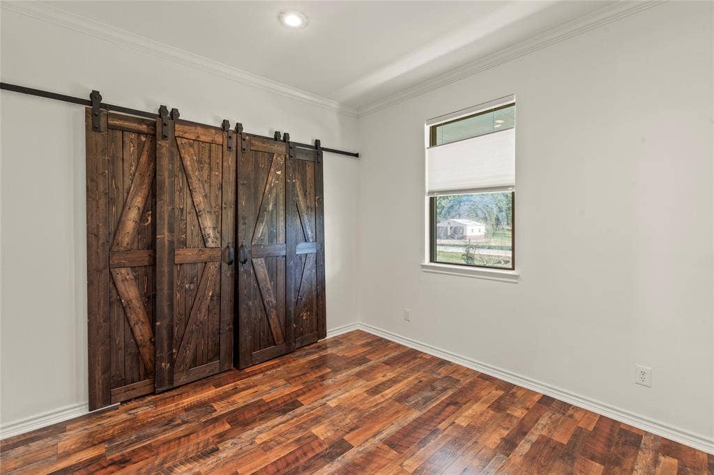 409 Oak Creek Drive, Tool, TX 75143 Ensuite Bedroom One featuring wood-look flooring, natural light, and rustic sliding barn doors to closet.