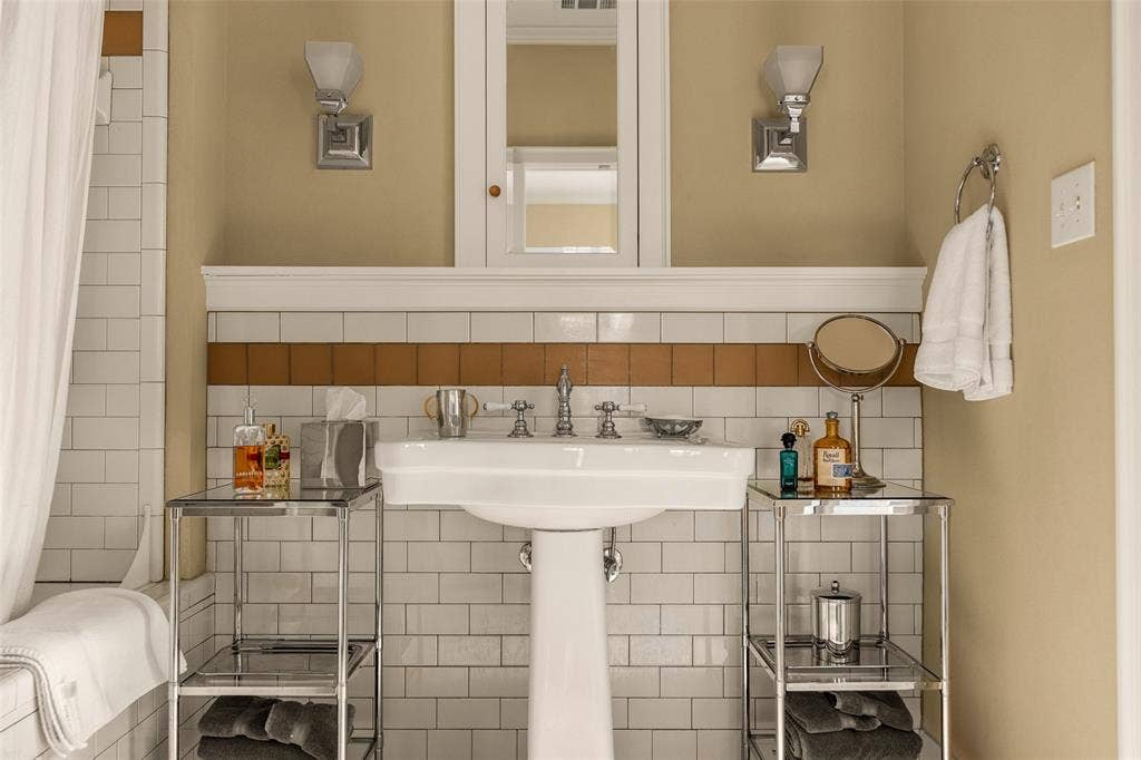 6020 Tremont Street, Dallas, TX 75214 Pedestal sink featuring chrome widespread faucet hardware, subway tile wall cladding with a decorative tile accent band, built-in medicine cabinet, and dual wall-mounted light fixtures
