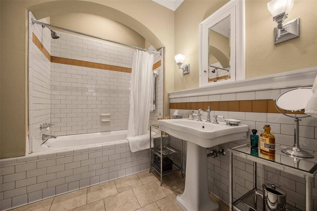 6020 Tremont Street, Dallas, TX 75214 Bathroom featuring a pedestal sink, arched shower alcove, subway tile walls with horizontal decorative accents, and tiled flooring