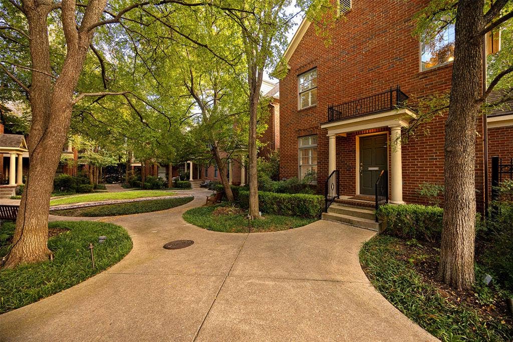 6020 Tremont Street, Dallas, TX 75214 Classic brick exterior featuring a covered portico, decorative iron balcony railing, stately columns, and mature landscaping