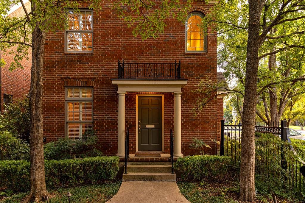 6020 Tremont Street, Dallas, TX 75214 Brick exterior featuring a covered entryway with structural columns, a wrought iron balcony, an arched window, and a paved walkway
