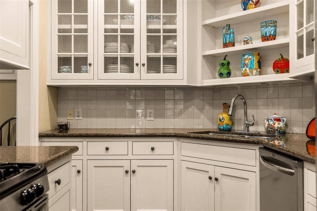 6020 Tremont Street, Dallas, TX 75214 White cabinetry featuring glass-panel upper doors, open shelving, stone countertops, square-tile backsplash, and stainless steel sink hardware