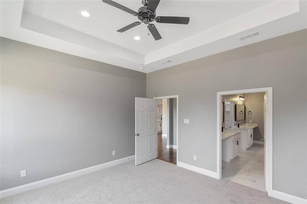10560 Lago Vista, Quinlan, TX 75474 Unfurnished bedroom with a tray ceiling, light carpet, a ceiling fan, connected bathroom, and recessed lighting