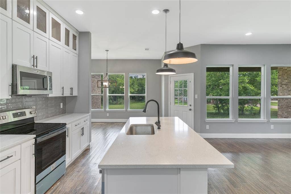 10560 Lago Vista, Quinlan, TX 75474 Kitchen with appliances with stainless steel finishes, an island with sink, white cabinets, light stone counters, and tasteful backsplash