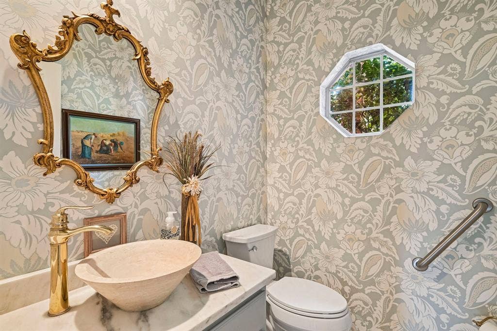 758 Livingston Drive, Allen, TX 75002 Powder room featuring decorative wallpaper, an ornate gold-finished wall mirror, a stone vessel sink, a metallic faucet, and an octagonal window