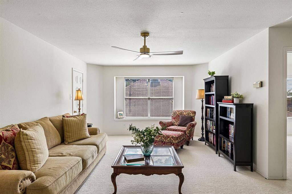 758 Livingston Drive, Allen, TX 75002 Living space featuring neutral carpeting, a large bay window, and a modern metallic finish ceiling fan with integrated lighting