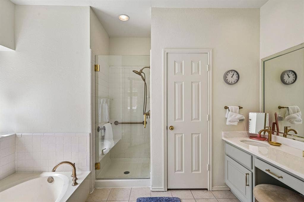 758 Livingston Drive, Allen, TX 75002 Bathroom featuring a drop-in soaking tub with a tiled surround, a walk-in glass-enclosed shower, dual-tone cabinetry with an integrated vanity, and brass-finish hardware
