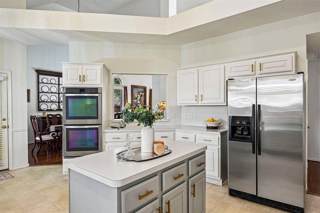 758 Livingston Drive, Allen, TX 75002 Kitchen featuring a center island, white cabinetry with brass-finish hardware, stainless steel side-by-side refrigerator, built-in double wall ovens, and vaulted ceilings