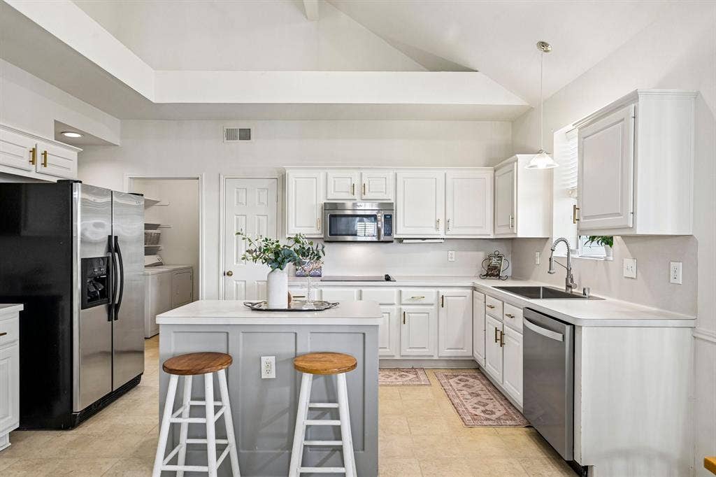 758 Livingston Drive, Allen, TX 75002 Kitchen featuring white cabinetry, a center island with a grey base, stainless steel appliances, solid surface countertops, and vaulted ceilings
