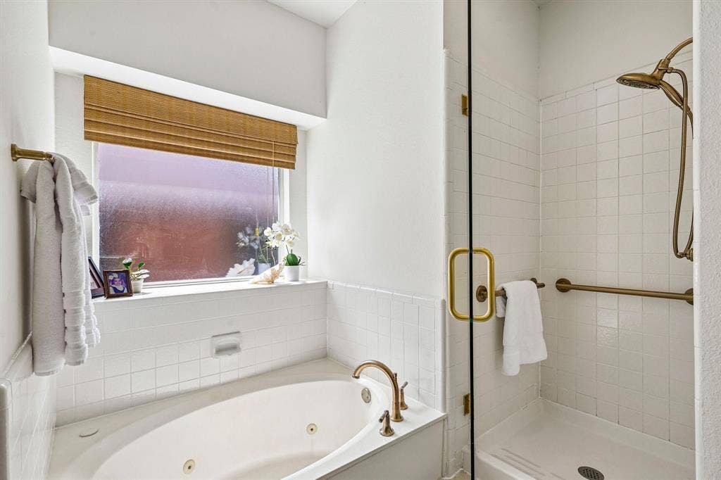 758 Livingston Drive, Allen, TX 75002 Jetted soaking tub and walk-in shower featuring brass-finish fixtures, white tile surround, and frameless glass enclosure