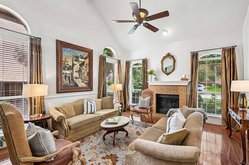 758 Livingston Drive, Allen, TX 75002 Vaulted ceilings featuring a central paddle fan, brick-surround fireplace with a mantel, polished wood-finish flooring, and multiple arched windows