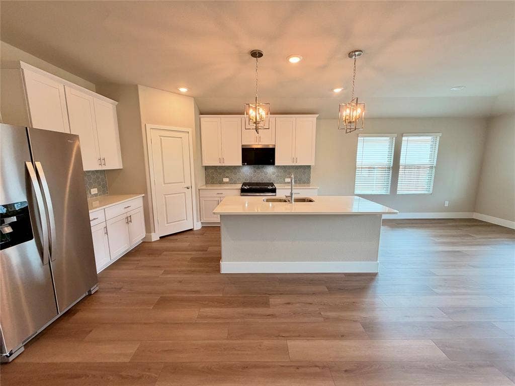 Kitchen featuring white cabinetry, wood-finish flooring, a central island with a solid-surface countertop, stainless steel appliances, and dual pendant lighting