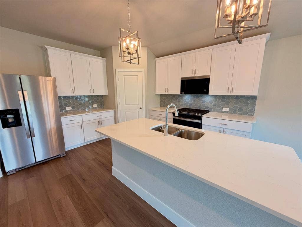 Kitchen featuring white cabinetry, an expansive central island with a quartz countertop, wood-finish flooring, a stainless steel refrigerator, and a geometric-patterned backsplash