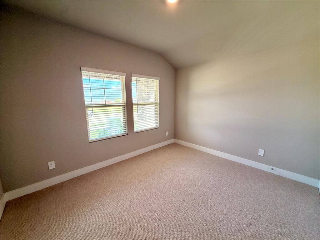 Neutral-toned room featuring a vaulted ceiling, wall-to-wall carpeting, and double windows with installed blinds