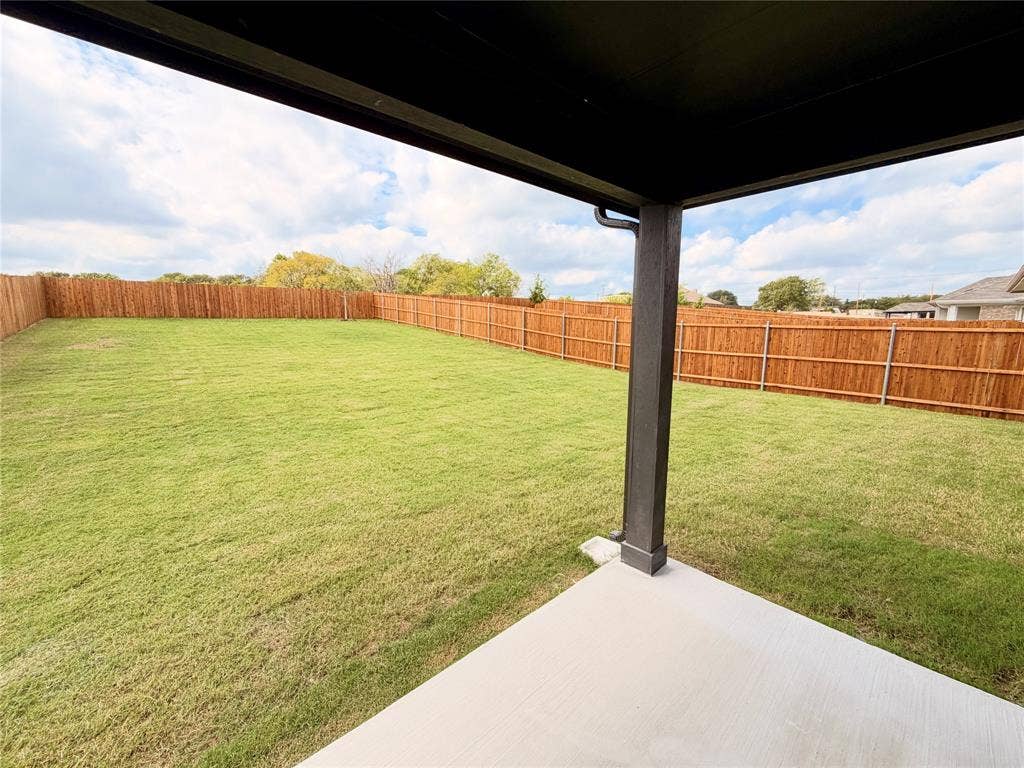 Covered concrete patio overlooking an expansive grass lawn enclosed by a tall wood privacy fence