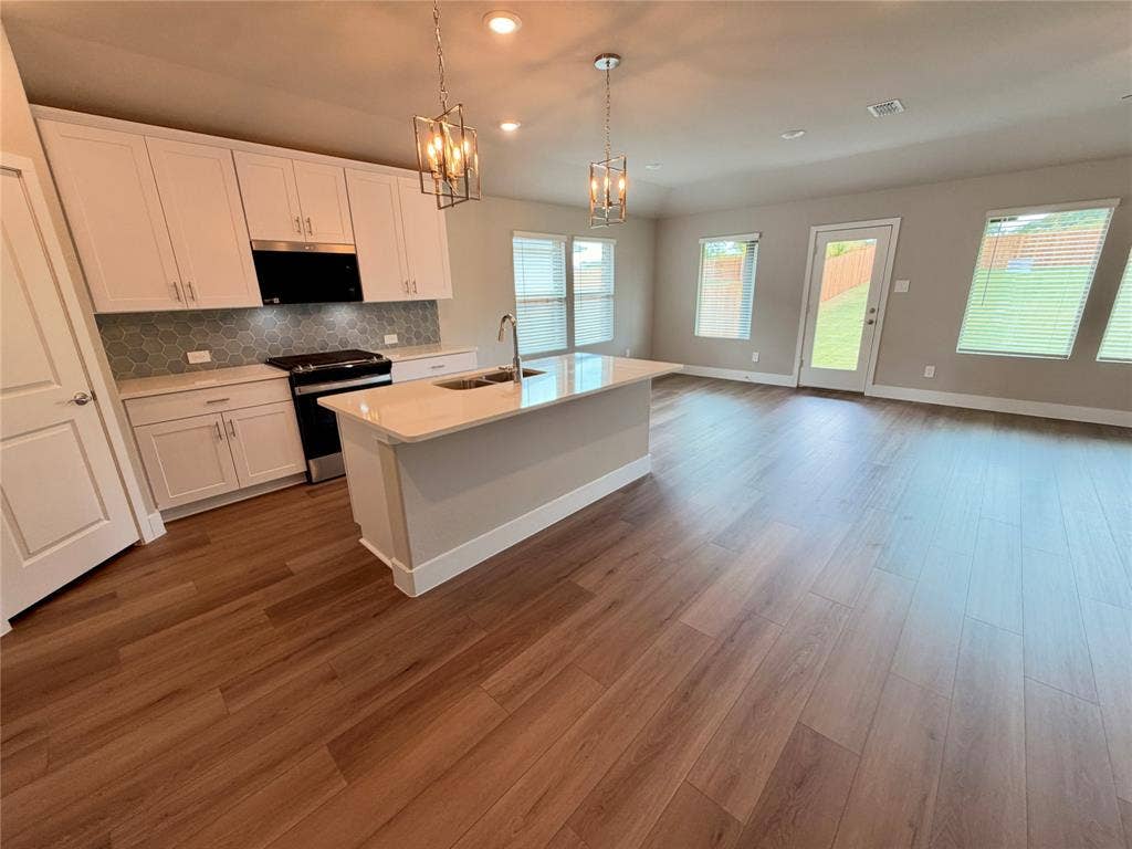 Kitchen featuring white shaker cabinetry, stone-finish countertops, geometric tile backsplash, wood-finish flooring, and dual pendant lighting