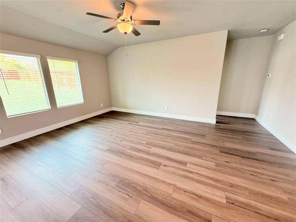 Room featuring vaulted ceilings, wood-finish flooring, dual windows with blinds, and a central ceiling fan