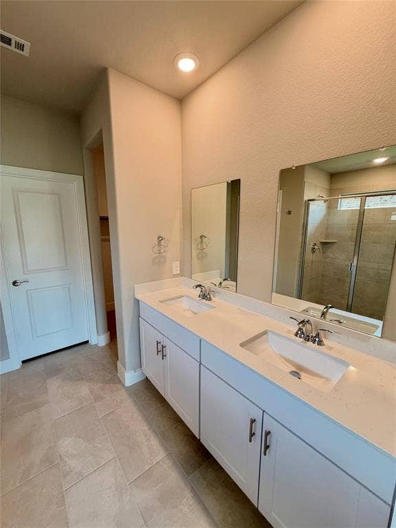 Double vanity featuring white cabinetry, light-toned stone-finish countertops, dual under-mount sinks, and large frameless mirrors