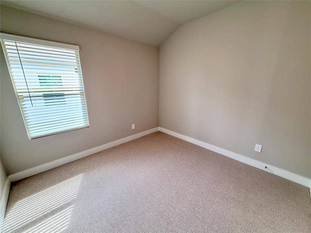 Room featuring neutral-toned carpeting, vaulted ceilings, and a window with horizontal blinds