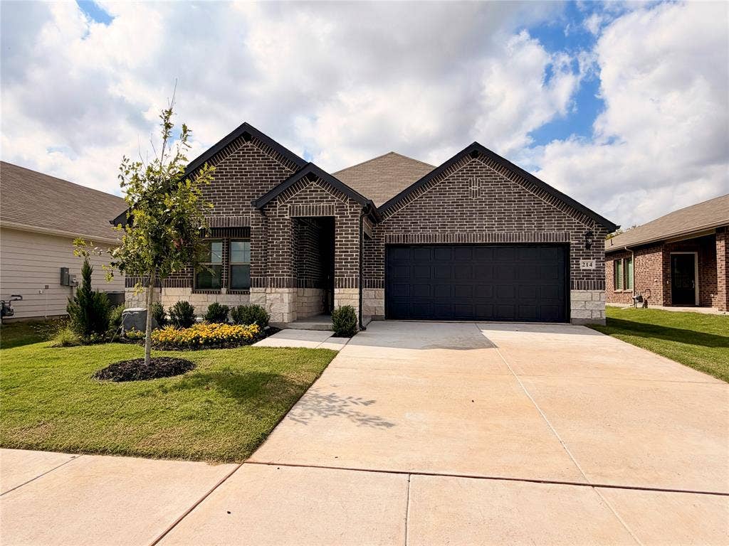 Exterior facade featuring dark brick masonry with light-toned stone accents, a concrete driveway, two-car garage, and manicured landscaping