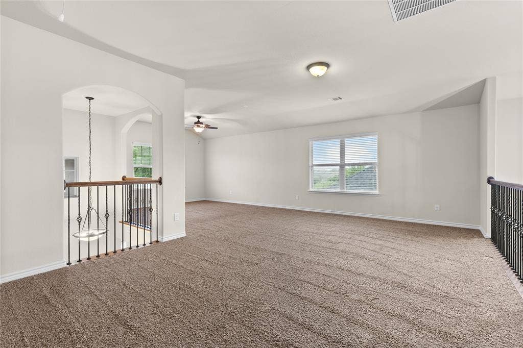 5751 Mountain Hollow Drive, Dallas, TX 75249 Expansive open-concept space featuring vaulted ceilings, neutral wall tones, carpeted flooring, wrought-iron staircase railing, and a decorative arched entryway