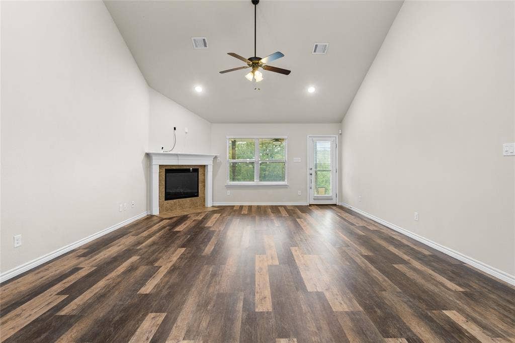 5751 Mountain Hollow Drive, Dallas, TX 75249 Vaulted ceiling living area featuring wood-finish flooring, a fireplace with a white mantel, a ceiling fan with integrated lighting, and glass-paneled exterior door