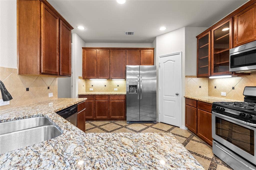 5751 Mountain Hollow Drive, Dallas, TX 75249 Kitchen featuring natural wood cabinetry, stone-finish countertops, stainless steel appliances, a tile backsplash with decorative accents, and tile flooring with diamond-pattern detailing