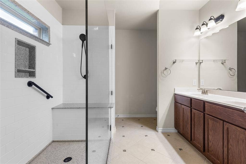 5751 Mountain Hollow Drive, Dallas, TX 75249 Walk-in shower with a glass enclosure, built-in stone-top bench, and matte black hardware, paired with a wood-finish dual-sink vanity and tiled flooring