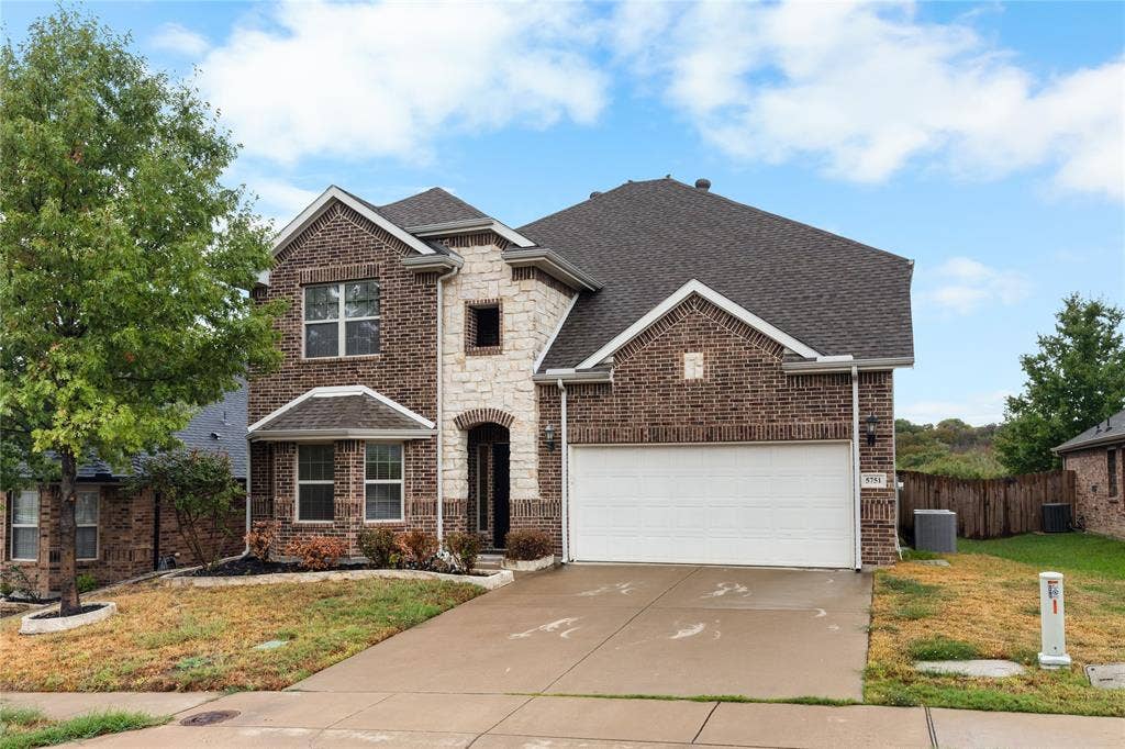 5751 Mountain Hollow Drive, Dallas, TX 75249 Two-story exterior featuring a brick and stone facade, a multi-gabled roofline, and an attached two-car garage with a concrete driveway