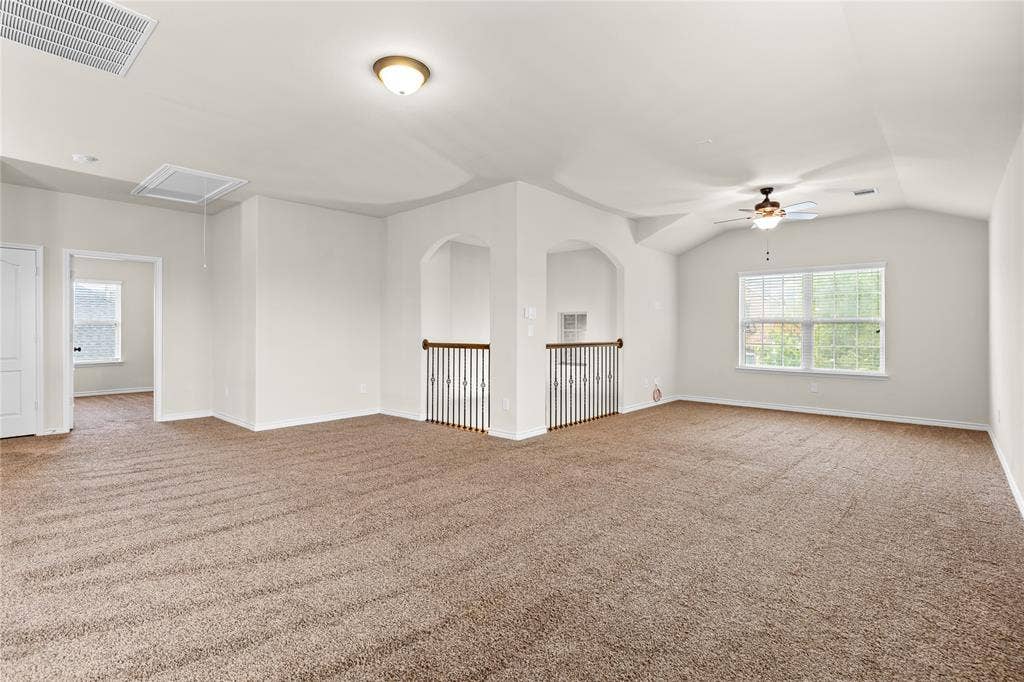 5751 Mountain Hollow Drive, Dallas, TX 75249 Expansive carpeted room featuring vaulted ceilings, arched entryways, metal spindle railings, and an integrated ceiling fan with lighting