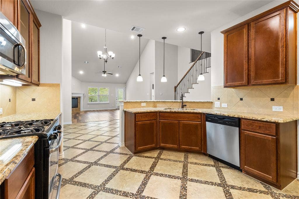 5751 Mountain Hollow Drive, Dallas, TX 75249 Kitchen featuring stained wood cabinetry, stone-patterned countertops, geometric-patterned tile flooring, stainless steel appliances, and triple pendant lighting