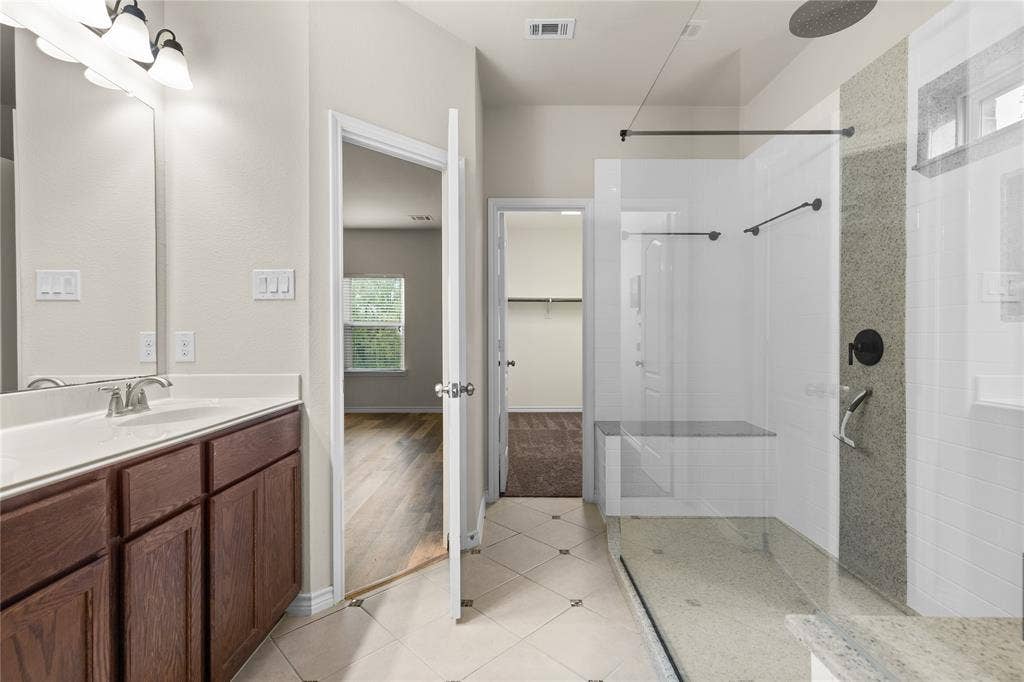 5751 Mountain Hollow Drive, Dallas, TX 75249 Bathroom featuring a vanity with wood-finish cabinetry, a white countertop with an integrated sink, and a walk-in shower with a glass enclosure, a stone-tile accent wall, and a built-in bench