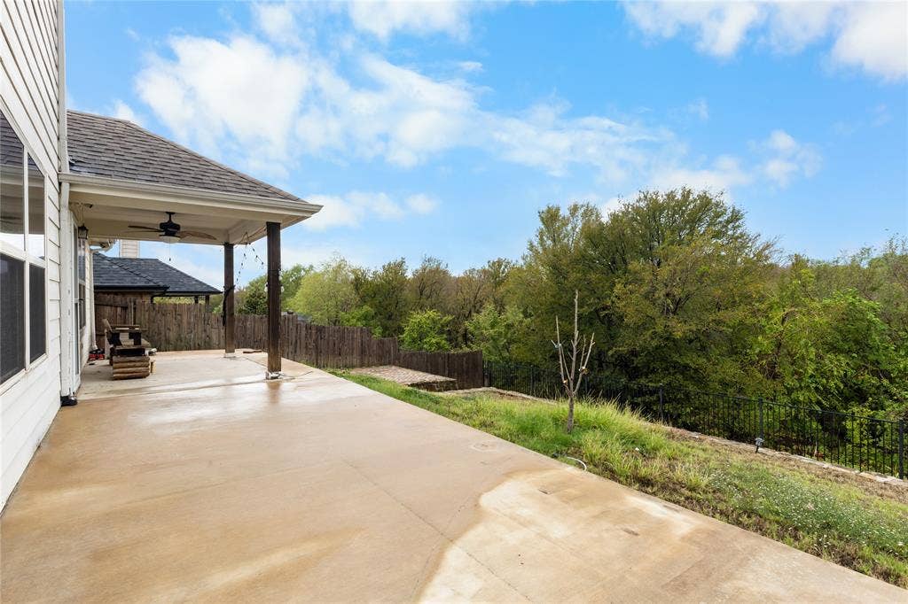 5751 Mountain Hollow Drive, Dallas, TX 75249 Covered concrete patio featuring a ceiling-mounted fan and an open backyard with wood fencing and mature trees