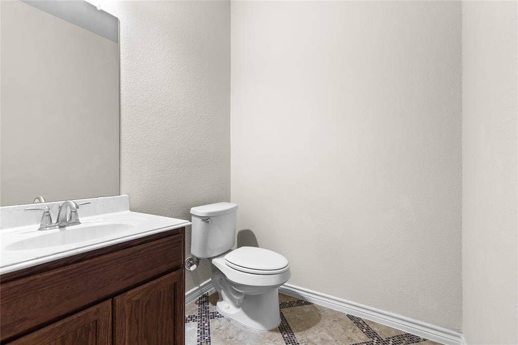 5751 Mountain Hollow Drive, Dallas, TX 75249 Bathroom featuring a wood-finish vanity with a light-toned countertop, integrated oval sink, chrome-finish widespread faucet, and decorative tile flooring with mosaic accents