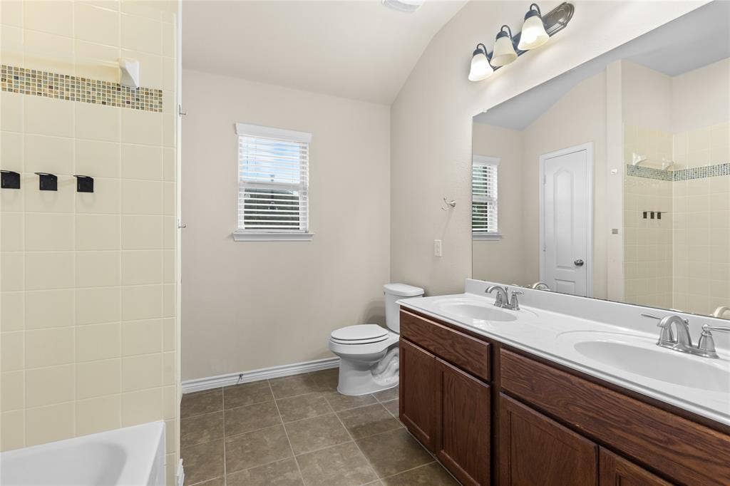 5751 Mountain Hollow Drive, Dallas, TX 75249 Bathroom featuring a double vanity with integrated sinks, large wall-mounted mirror, ceramic tile flooring, and a shower-tub combination with tiled surround