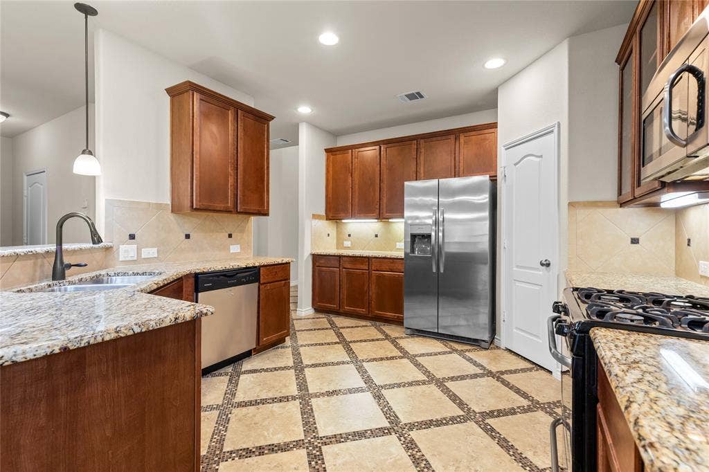 5751 Mountain Hollow Drive, Dallas, TX 75249 Kitchen featuring wooden cabinetry, stone-surface countertops, tile backsplash with decorative accents, stainless steel appliances, and tile flooring with a geometric inlay pattern