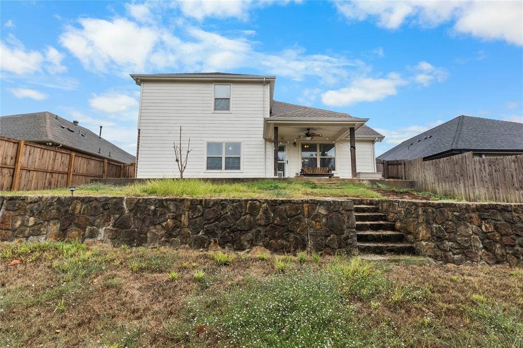 5751 Mountain Hollow Drive, Dallas, TX 75249 Rear exterior featuring a two-story light-colored siding facade, a covered patio with dark support pillars, and a stone retaining wall with built-in stone steps