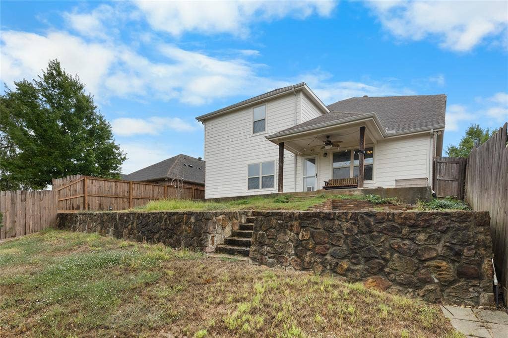 5751 Mountain Hollow Drive, Dallas, TX 75249 Two-story light-colored siding exterior featuring a covered patio, tiered natural stone retaining wall, integrated stone staircase, and wood privacy fencing