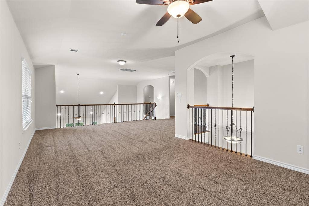 5751 Mountain Hollow Drive, Dallas, TX 75249 Open interior space featuring vaulted ceilings, neutral wall-to-wall carpeting, metal spindle railings, and a central ceiling fan