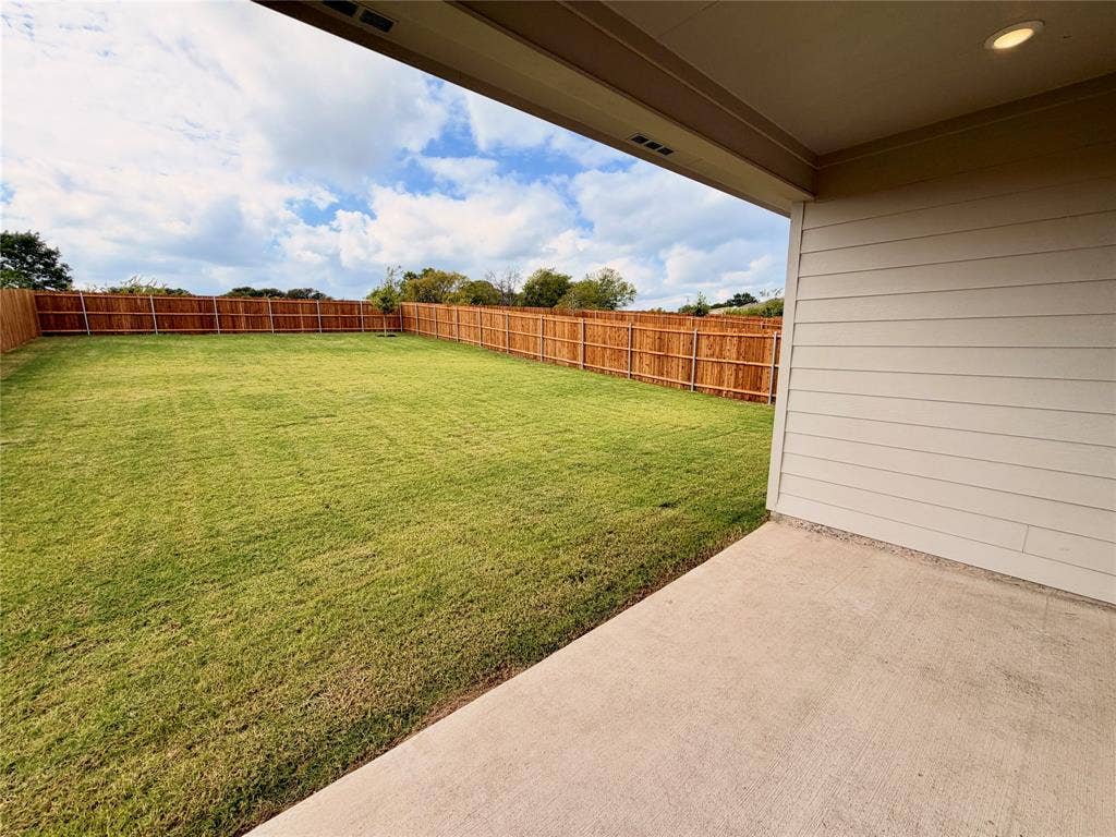 Covered concrete patio with horizontal siding exterior, expansive lawn, and wooden privacy fencing