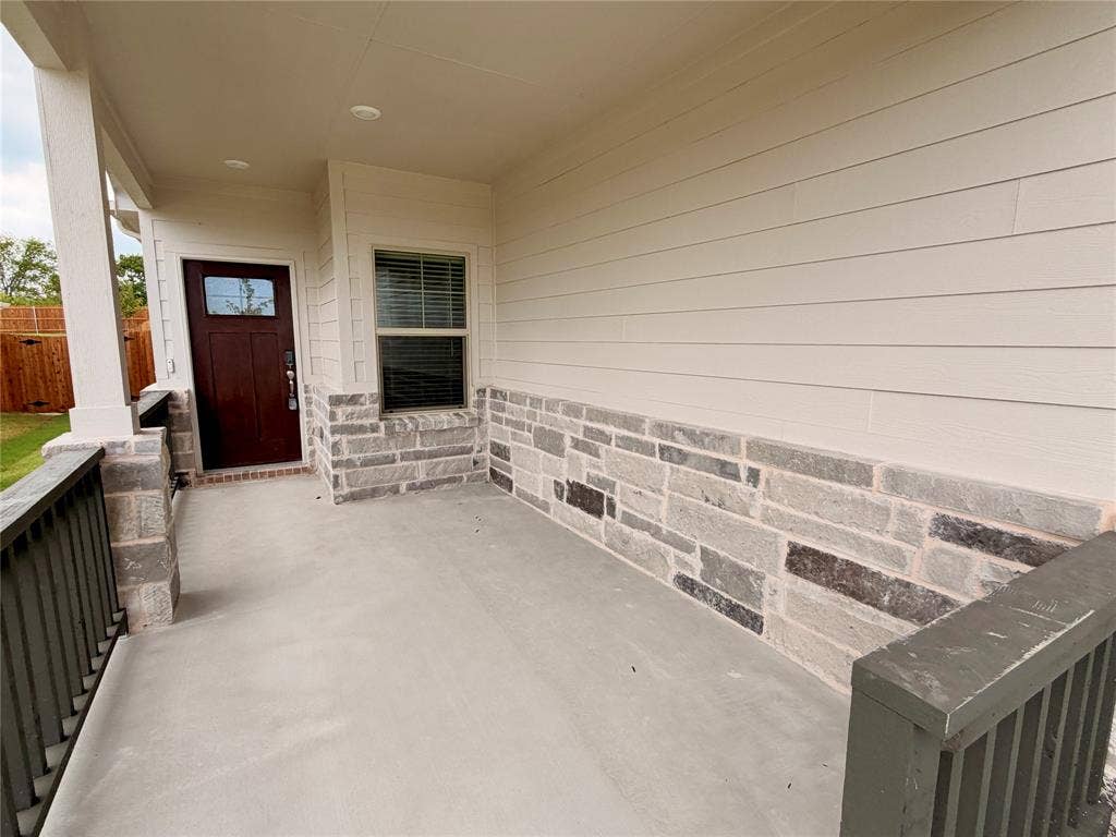 Covered front porch featuring concrete flooring, a multi-pane glass-panel entry door, horizontal lap siding, and stone veneer accents