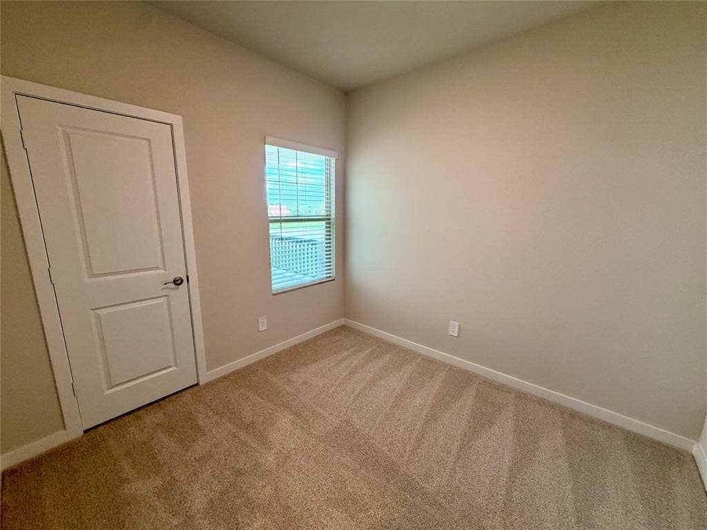 Neutral-toned room featuring neutral-toned carpeting, a single-panel interior door with a brushed nickel handle, and a multi-pane window with horizontal blinds