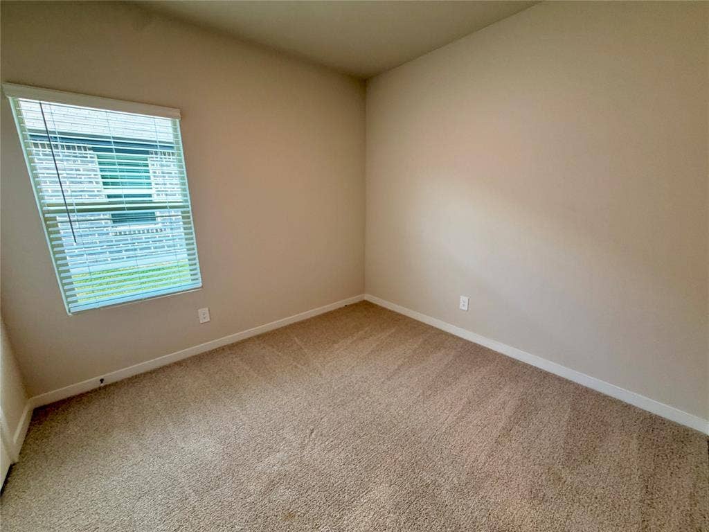 Neutral-toned interior space featuring neutral wall paint, wall-to-wall carpeting, and a window fitted with horizontal blinds