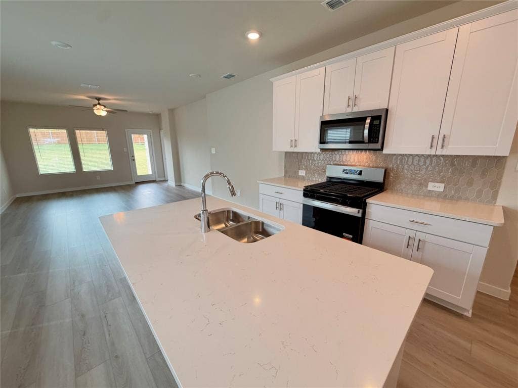 Kitchen featuring a central island with a quartz countertop and stainless steel undermount sink, shaker-style cabinetry, patterned tile backsplash, and recessed lighting