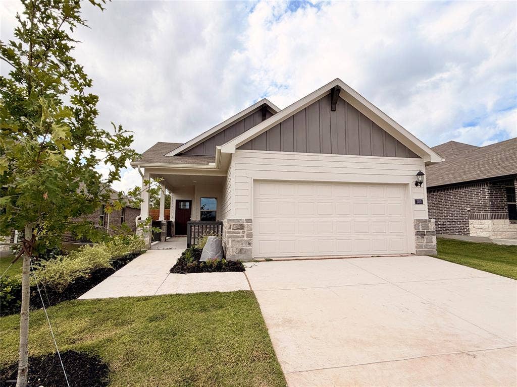 Single-story exterior featuring a mix of horizontal siding and vertical board-and-batten siding, stone masonry accents, a front-facing attached garage, and a covered entryway