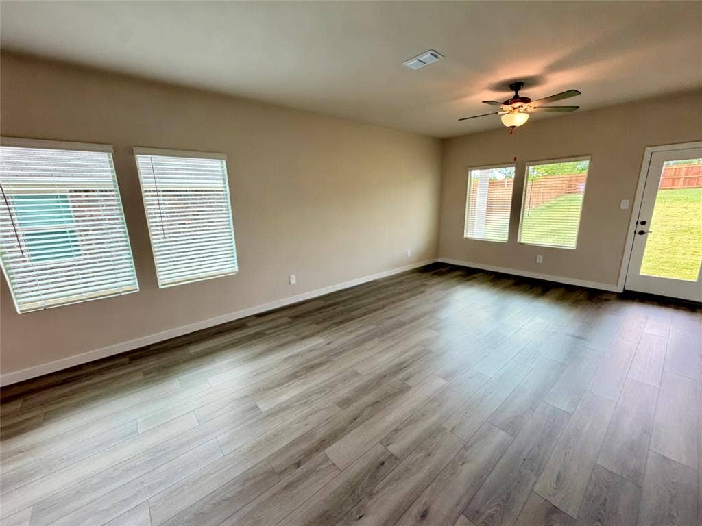 Living area featuring wood-finish flooring, neutral wall tones, multiple windows, a ceiling fan with light fixture, and a glass-panel exterior door