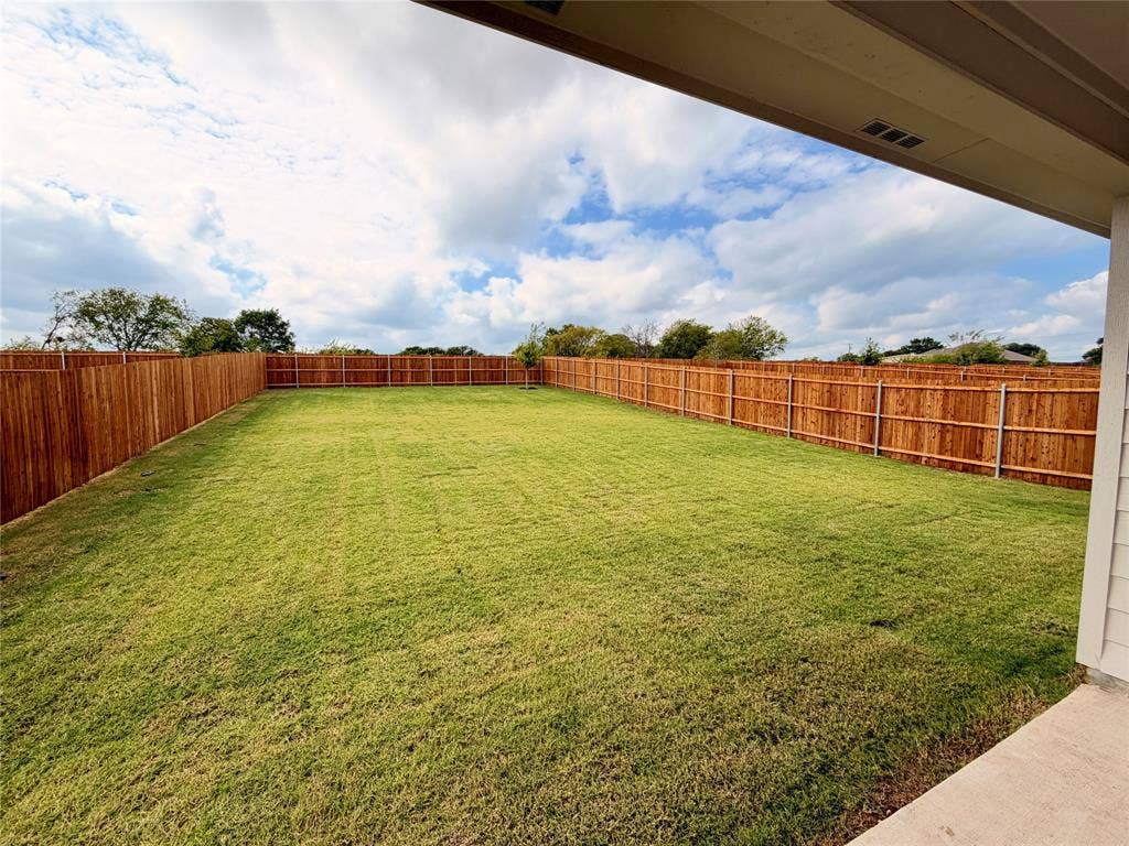 Backyard featuring a concrete patio, grass lawn, and full-perimeter wood privacy fencing